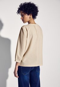 Top beige con motivo, con maniche a tre quarti, tessuto a griglia testurizzato, scollatura rotonda e vestibilità comoda, abbinato a jeans blu scuro.