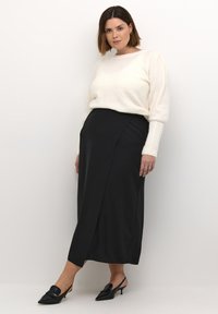 Crèmekleurige trui met pofmouwen, gecombineerd met een hoog-waisted zwarte rok met een split aan de zijkant. Zwarte slingback schoenen met een strikdetail.