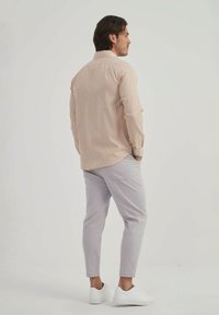 Chemise rayée beige clair à manches longues, associée à un pantalon gris clair ajusté et des chaussures blanches à enfiler, vue de dos.