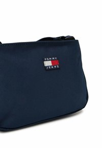 Borsa in nylon blu navy con superficie testurizzata, caratterizzata da una patch rettangolare con il logo Tommy Jeans in rosso, bianco e blu. Chiusura con zip.