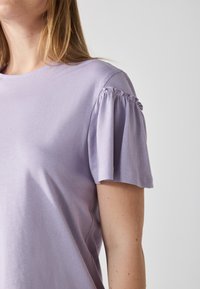 Top corto a maniche corte di un viola chiaro in cotone morbido, con dettagli arricciati sulle maniche e un classico scollo rotondo.