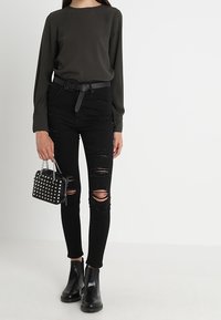Black long-sleeve top, fitted black ripped skinny jeans, black ankle boots, and a small black studded handbag with chain strap.