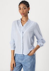 Camicia a bottoni a righe blu con colletto arruffato e dettaglio plissettato sul davanti. Maniche lunghe arrotolate con polsini elasticizzati. Tessuto testurizzato.