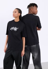 Svart t-shirt med en grafisk design som har ett cirkulärt element. Tyget ser slätt ut, med korta ärmar och en avslappnad passform.