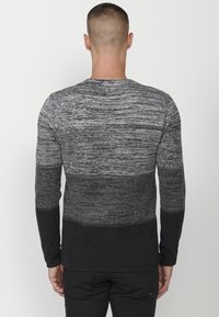 Pulover tricotat cu mânecă lungă, având un gradient de nuanțe de gri, cu un material texturat și o secțiune inferioară solidă, de culoare neagră. Guler rotund, croială ajustată.