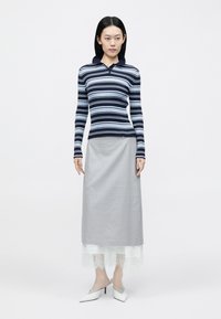 Πλεκτό πόλο μπλουζάκι ριγέ σε ναυτικό και ανοιχτό μπλε χρώμα με γιακά, συνδυασμένο με μια γκρι μάξι φούστα με δαντελένιο τελείωμα και λευκές γόβες με μυτερή μύτη.