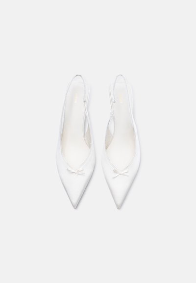 Paire de ballerines blanches à bout pointu avec brides arrière et petits nœuds décoratifs sur un fond blanc uni.