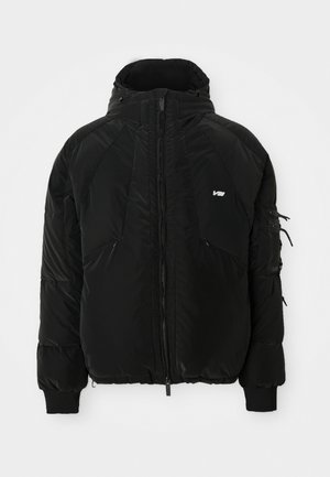 Black puffer jacket with a high collar, front zipper, and two front pockets. Additional details include a zippered arm pocket and ribbed cuffs.