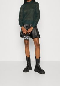 Grönmönstrad genomskinlig långärmad topp, svart läderflared kjol, svarta kraftiga ankelstövlar, liten handväska.