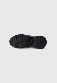 Black athletic shoe sole with a textured rubber tread. Features deep grooves and a curved design for enhanced grip and flexibility.