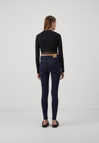Maglia nera a maniche lunghe con bordo in pizzo all'orlo, abbinata a jeans skinny blu scuro con una piccola etichetta e due tasche posteriori.