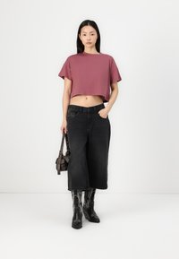 Rövidített, bordó színű póló, laza fekete farmer culotte, fekete cowboy csizma fehér hímzéssel, egy kis barna kézi táskával.