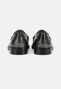 Pantofi din piele patentată neagră cu un finisaj neted, toc mic și două curele cu catarame. Vedere din spate, evidențiind designul elegant.