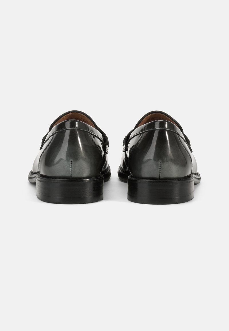 Schwarze Lacklederschuhe mit glatter Oberfläche, niedrigem Absatz und doppelten Riemen mit Schnallen. Ansicht von hinten, die das schlanke Design hervorhebt.