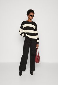 Maglione a righe bianche e nere con una vestibilità ampia, abbinato a pantaloni neri a vita alta e stivaletti neri, mentre tiene una borsa bordeaux.