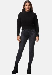 Svart stickad kort tröja med ett strukturerat mönster, tillsammans med mörka slim fit jeans och svarta ankelboots med kraftig klack.