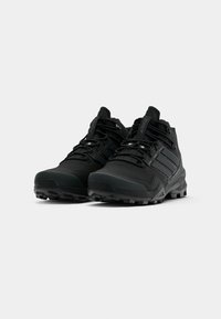 Ein Paar schwarze, hochgeschnittene Sportschuhe mit strukturierten Sohlen und Schnürdesign auf einem schlichten weißen Hintergrund.