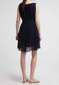 Laivastonsininen pleatimekko, jossa on hihaton malli, vartalonmyötäinen vyötärö ja ilmava A-linjainen helma. Kevyt kangas, jossa on herkkä rakenne.