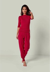 Rotes Strickoberteil mit hohem Ausschnitt und kurzen Ärmeln, kombiniert mit roten, locker sitzenden Hosen mit elastischem Bund und Bündchen.