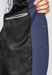 Navyblaues Sakk-Futter mit schwarzem Satin, einer weißen Streifen-Tasche und einem seitlichen Schlitz mit sichtbaren Nähten.