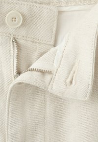 Bežové džíny z denimu rozepnuté, se viditelným stříbrným zipem, zapínáním na knoflík a knoflíkovou dírkou na pase.