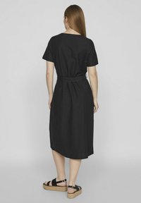 Juodas trumpomis rankovėmis suknelė su prispausta talija. Iki kelių, laisvas fasonas. Modelis vilki platforminius sandalus su juodais raišteliais ir pintais padais.