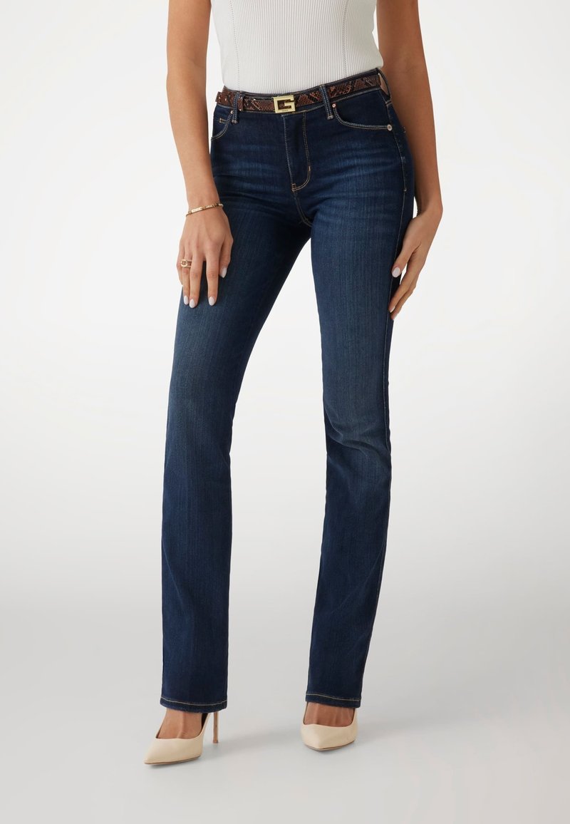 Dark blue denim jeans with a straight-leg cut, featuring a patterned brown belt with a gold buckle and five pockets, worn with beige heels.