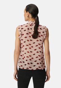 Roze mouwloos blouse met ruffles op de schouders, versierd met een herhaalde rode lippenprint, afgewerkt met een knoopsluiting aan de achterkant van de nek.