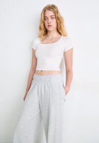 Witte, geknipte, strakke geribbelde T-shirt met een vierkante halslijn, gecombineerd met lichtgrijze, losse sweatpants met een elastische tailleband.