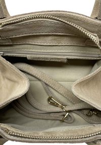 Beige semišová kabelka uvnitř s kapsou na zip, tkaninovou podšívkou a odnímatelným popruhem. Viditelné švy a kovové akcenty.