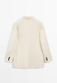 Kremowa damska marynarka widziana od tyłu, z długimi rękawami i czarnymi guzikami na mankietach.