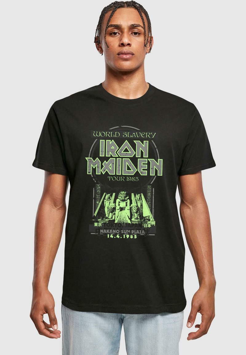 Tricou din bumbac negru cu un imprimeu grafic verde care afișează "Iron Maiden World Slavery Tour 1985" cu text stilizat și desene hieroglifice.