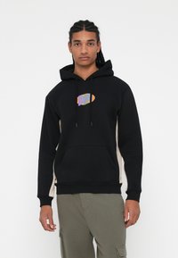 Sudadera con capucha negra, con un gráfico texturizado en el pecho, paneles laterales en contraste color beige y un bolsillo tipo canguro.