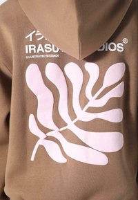 Brauner Hoodie mit pinkem Blattdesign auf der Rückseite. Mit weißem Text "IRASUTOS STUDIOS" und "ILLUSTRATED STUDIOS." Weicher Stoff.