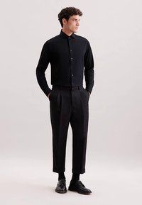 Camicia nera con bottoni, maniche lunghe, abbinata a pantaloni neri a vita alta. Caratteristiche: vestibilità aderente, tessuto liscio e design classico.