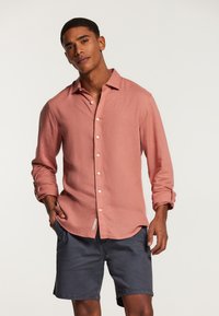 Chemise à manches longues rose clair avec des boutons, en tissu texturé, associée à un short marine foncé, avec une coupe décontractée et un ourlet arrondi.