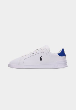 Zapatilla blanca de media caña con lengüeta azul en el talón, cierre de cordones y logotipo negro de Polo Ralph Lauren en el lateral, sobre un fondo liso.