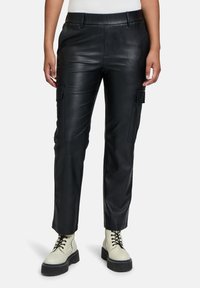 Zwarte leren cargobroek met een aansluitend ontwerp, voorzien van zijzakken en een gladde textuur, gecombineerd met chunky crèmekleurige laarzen.