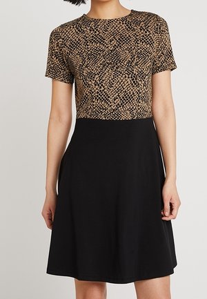 Kvinde iført en kortærmet kjole med en brun og sort slangeprint-top og et ensfarvet sort A-formet skørt.