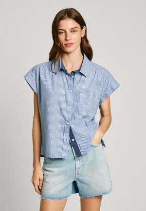 Blau-weiße gestreifte kurzärmelige Hemd mit Knopfleiste und Tasche, getragen mit hellen Jeansshorts. Der Stoff wirkt glatt und atmungsaktiv.