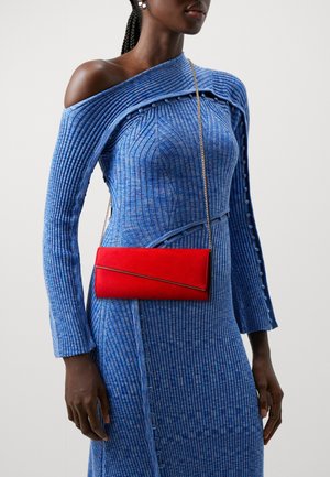 Rød ruskinds flap taske med et guldaccent, båret som crossbody, parret med en blå ribbet kjole med off-shoulder design og knapdetaljer.