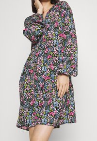 Kukkamekko mustalla pohjalla, jossa on eloisat vaaleanpunaiset, siniset ja vihreät kuviot. V-kaula-aukko, pitkät hihat ja väljä malli. Kevyt kangas.