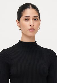 Haut en tricot noir à côtes avec un col montant, doté de longues manches et d'une silhouette ajustée. Design simple, sans motifs ni embellissements visibles.