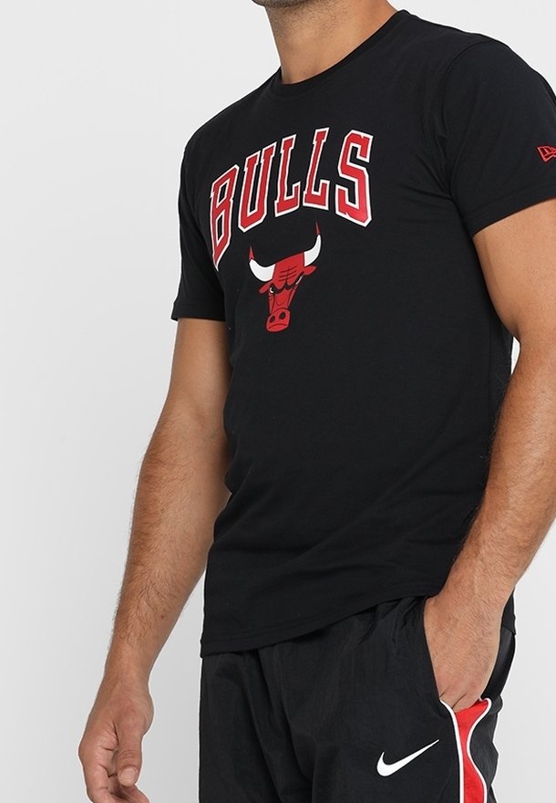 Mann in einem schwarzen Chicago Bulls T-Shirt mit rotem und weißem Logo und schwarzen Nike Shorts mit rotem und weißem Streifen, die Hand in der Tasche.