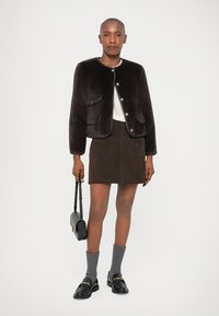 Brun faux fur jakke med gullknapper, stylet over en hvit topp, parret med et brunt semsket skinnskjørt, grå sokker og svarte loafers.