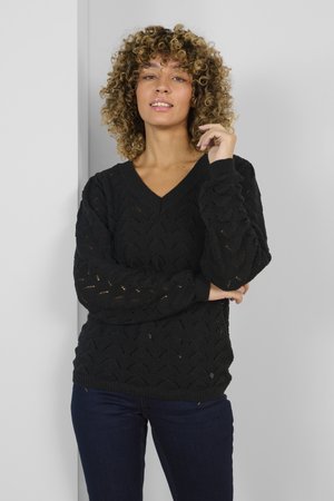 Pulover negru tricotat, cu decolteu în V, model cu ochi de plasă, mâneci texturate și manșete cu nervuri, purtat cu blugi negri.