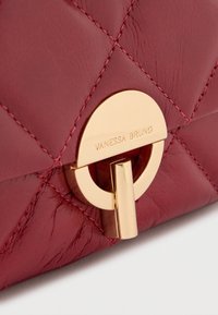 Κόκκινη δερμάτινη τσάντα με καπιτονέ σχέδιο και χρυσό στρογγυλό κλείσιμο με χαραγμένο το "Vanessa Bruno." Ομαλή υφή και αντίθετες ραφές λεπτομέρειες.