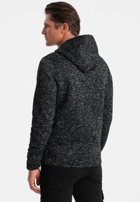 Dunkelgrauer Hoodie mit einem strukturierten, marmorierten Muster. Verfügt über eine Kapuze und lange Ärmel und besteht aus einem weichen, gestrickten Stoff.