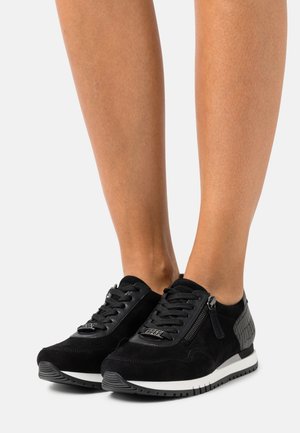 Zapatillas de ante negro con un panel texturizado negro en el talón, suela blanca en contraste y un detalle con cremallera en el lado.