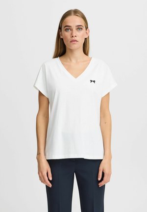 Hvid V-hals t-shirt lavet af bomuld, med korte ærmer og et lille sort bue-emblem på venstre bryst. Glat tekstur.